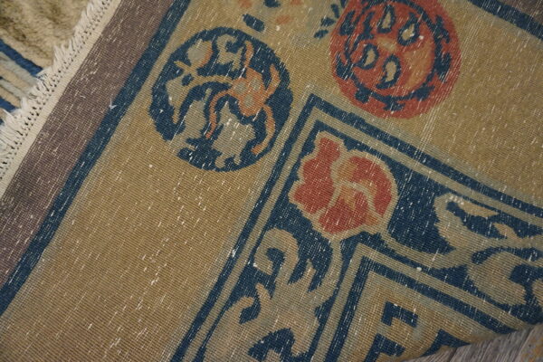 Low-pile tan rug with detailed navy and rust floral patterns and visible white fringed edge.