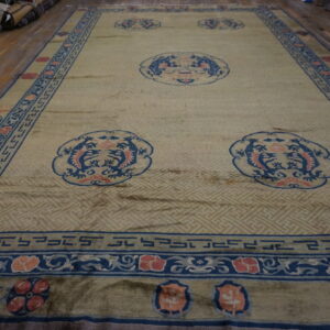 A large gold and beige rug with blue and coral medallions covers a wood floor near stacked rolls.