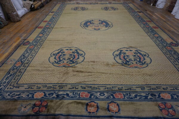A large gold and beige rug with blue and coral medallions covers a wood floor near stacked rolls.
