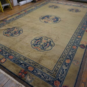 Muted gold rug featuring blue and coral dragon motifs surrounded by intricate borders on wide wood planks.
