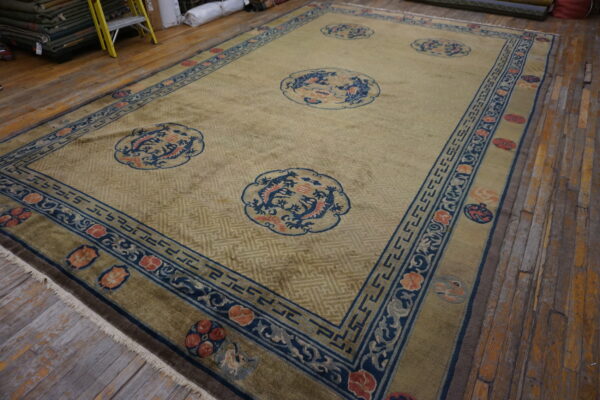 Muted gold rug featuring blue and coral dragon motifs surrounded by intricate borders on wide wood planks.