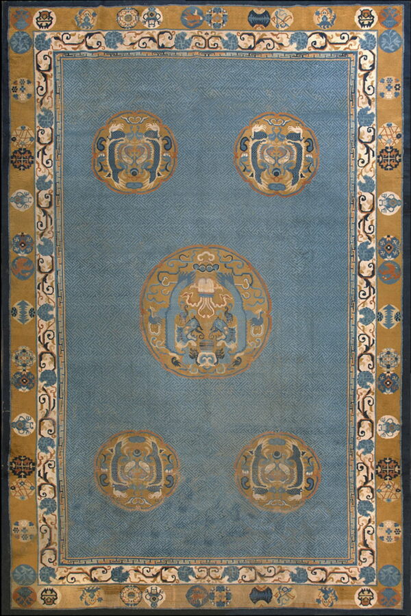 A large blue and gold rug featuring a field of subtle key patterns and five detailed roundel medallions.