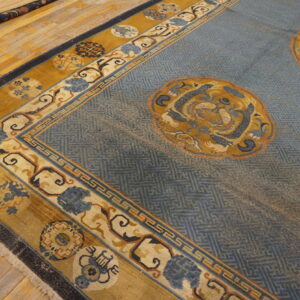 Low-pile blue rug with repeating lattice pattern, gold medallions, and ornate borders on wood flooring.