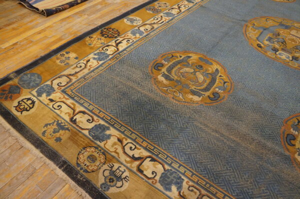 Low-pile blue rug with repeating lattice pattern, gold medallions, and ornate borders on wood flooring.