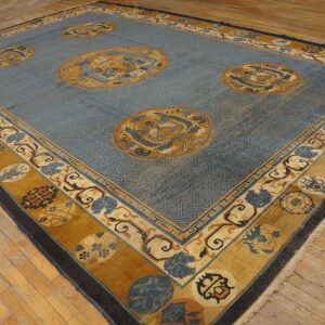Distressed blue rug with gold medallions, a geometric field pattern, and a wide ornate border on light wood floors.