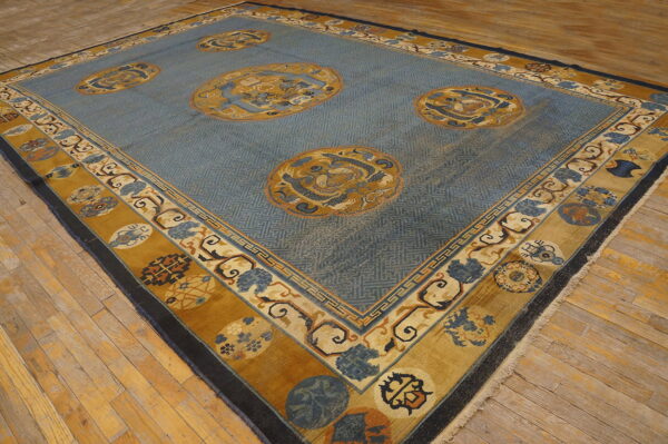 Distressed blue rug with gold medallions, a geometric field pattern, and a wide ornate border on light wood floors.