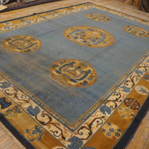 A wide blue rug with gold and cream borders and medallion designs rests on light wood planks.