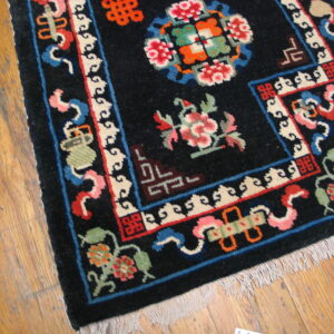 Black high-pile rug with colorful floral and geometric patterns shown on distressed light brown hardwood.