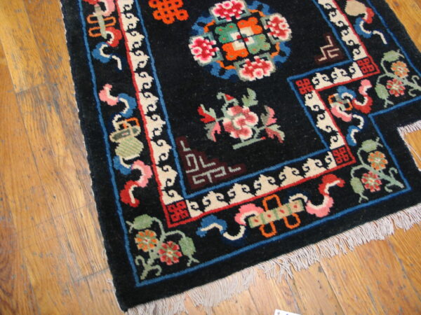 Black high-pile rug with colorful floral and geometric patterns shown on distressed light brown hardwood.