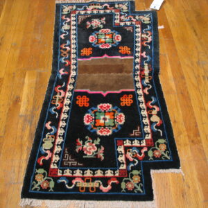 Black rug with a stepped edge, colorful repeating patterns, and a brown center stripe on wood planks.