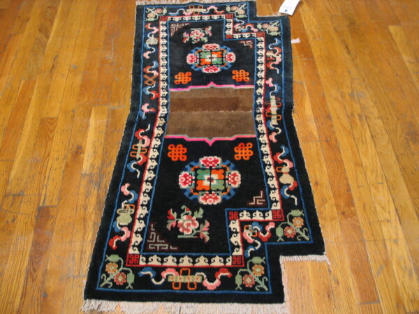 Black rug with a stepped edge, colorful repeating patterns, and a brown center stripe on wood planks.