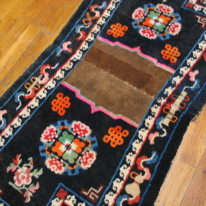 A black runner rug with bright floral and geometric motifs, featuring a solid brown patch on wood flooring.