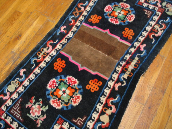 A black runner rug with bright floral and geometric motifs, featuring a solid brown patch on wood flooring.