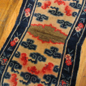 Low-pile tan and navy rug featuring red and blue cloud motifs on golden hardwood floors.
