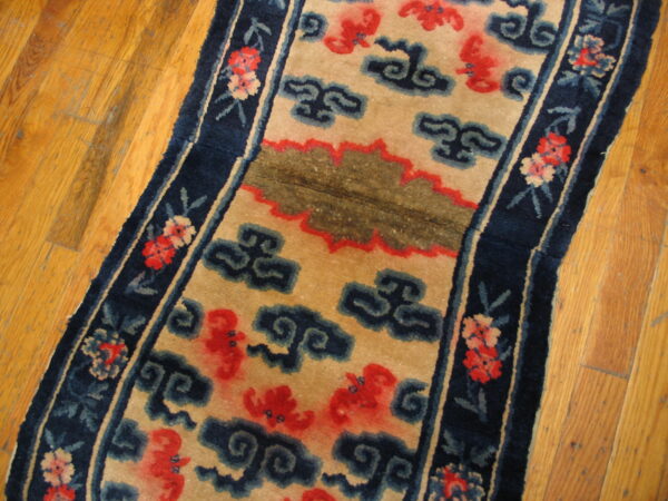 Low-pile tan and navy rug featuring red and blue cloud motifs on golden hardwood floors.
