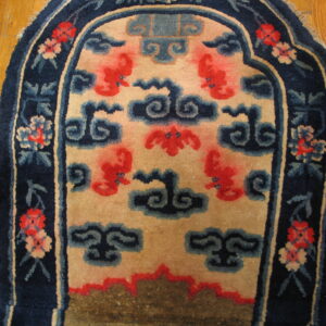 Arched navy rug with a floral border and red stylized figures on a tan field, resting on wood floor.