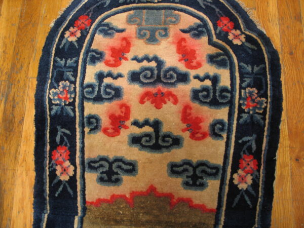 Arched navy rug with a floral border and red stylized figures on a tan field, resting on wood floor.