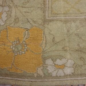 Textured rug corner showing mustard yellow and cream floral motifs on a chunky sage green pile over wood floor.