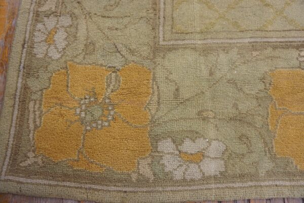 Textured rug corner showing mustard yellow and cream floral motifs on a chunky sage green pile over wood floor.