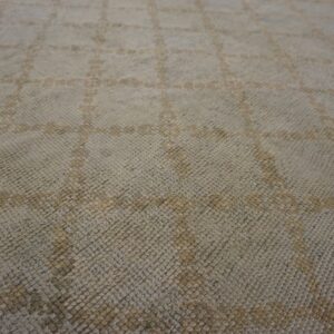 Close-up of a textured rug featuring a pale gray background and muted tan diamond grid pattern.