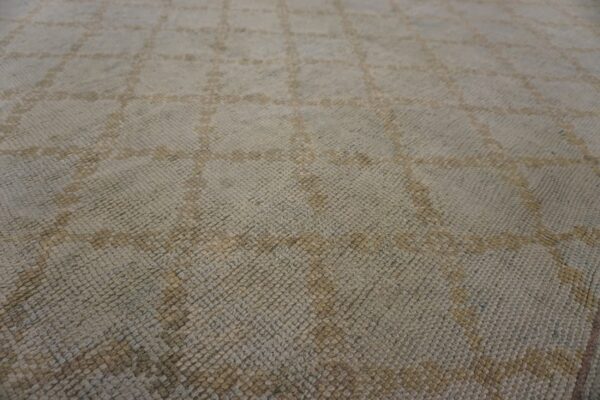 Close-up of a textured rug featuring a pale gray background and muted tan diamond grid pattern.