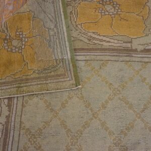 Folded low-pile rug with yellow floral and pale green geometric patterns resting on distressed wood floorboards.