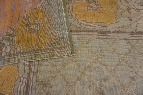 Folded low-pile rug with yellow floral and pale green geometric patterns resting on distressed wood floorboards.