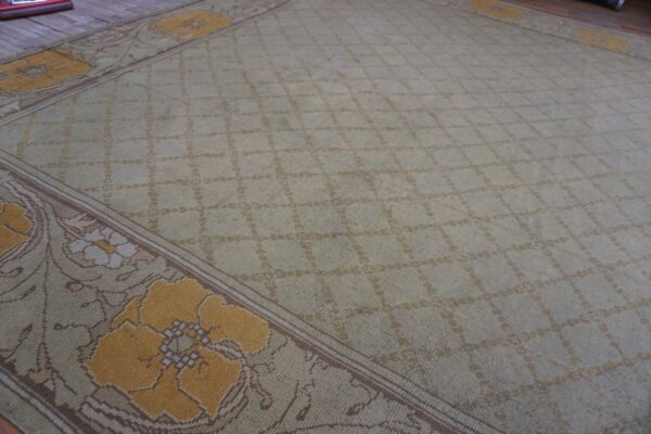 Low-pile sage rug featuring a lattice design and mustard yellow floral borders resting on wood floorboards.