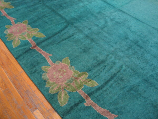 Close-up of a teal rug with a brown and mauve floral pattern over hardwood planks.