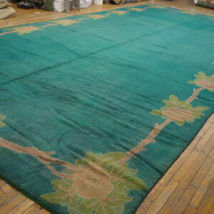 Large teal rug featuring a tan and green floral vine border lies on a distressed wood floor.