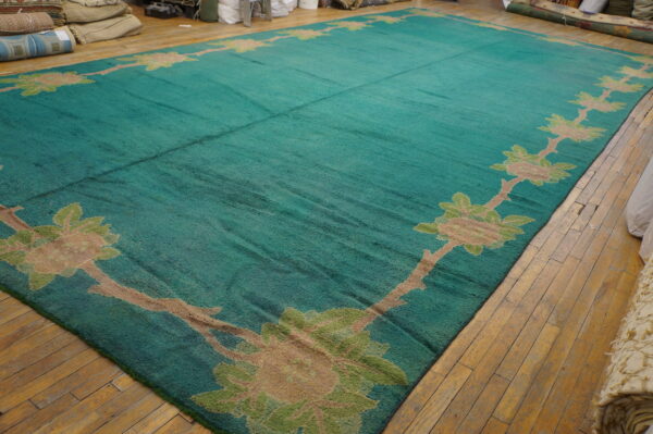 Large teal rug featuring a tan and green floral vine border lies on a distressed wood floor.