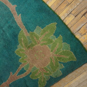 Teal rug with a floral pattern in green and tan rests on distressed light wood plank flooring.
