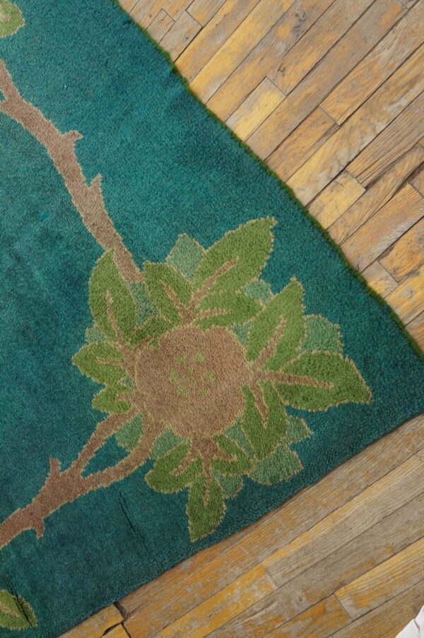Teal rug with a floral pattern in green and tan rests on distressed light wood plank flooring.