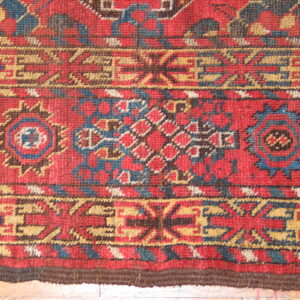 Detailed view of the rug's short pile texture and complex red, blue, and ochre geometric patterns.