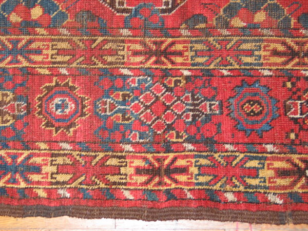 Detailed view of the rug's short pile texture and complex red, blue, and ochre geometric patterns.