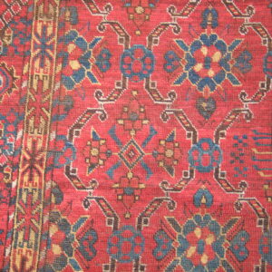 Red rug with a tight, woven texture, featuring stylized medallions and borders in blue, tan, and brown.