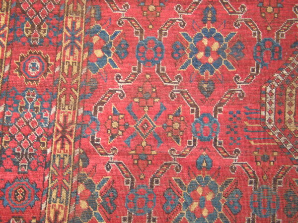 Red rug with a tight, woven texture, featuring stylized medallions and borders in blue, tan, and brown.