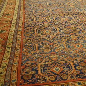 Navy blue and rust orange low-pile rug with detailed traditional patterns on light wood flooring.