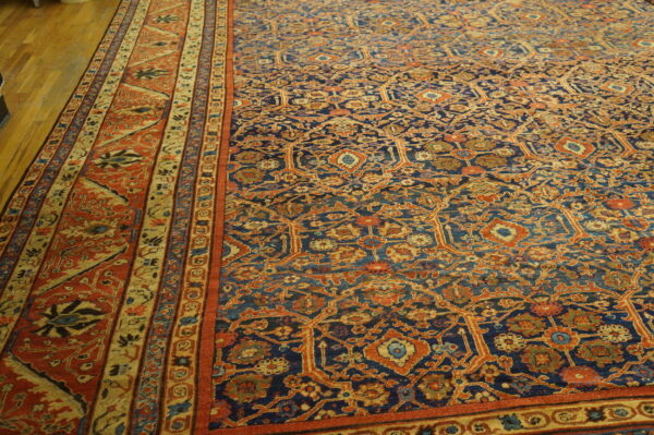 Navy blue and rust orange low-pile rug with detailed traditional patterns on light wood flooring.