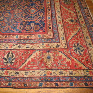 Intricate red and blue patterned rug with multiple tan and blue borders on wood flooring.
