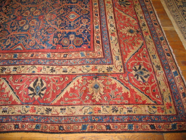 Intricate red and blue patterned rug with multiple tan and blue borders on wood flooring.