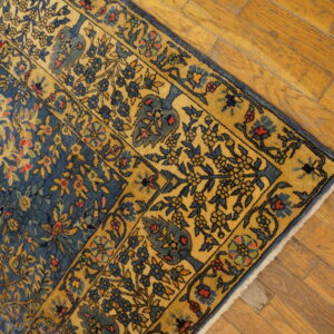 Angled view of a blue and gold traditional floral rug border resting on rustic honey-toned hardwood planks.