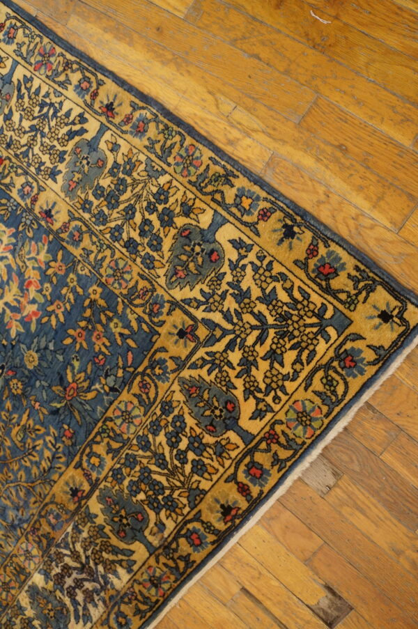 Angled view of a blue and gold traditional floral rug border resting on rustic honey-toned hardwood planks.