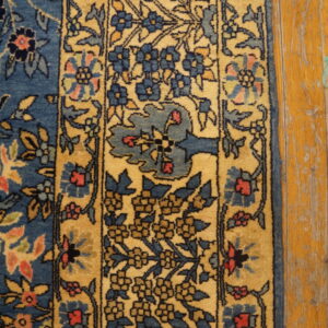 A blue and gold traditional floral rug border rests on worn wooden planks.