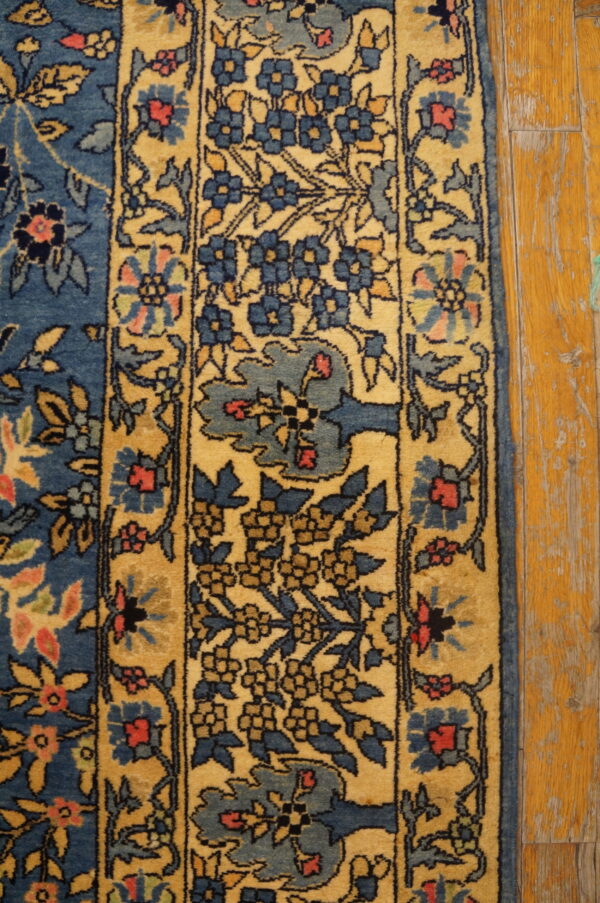 A blue and gold traditional floral rug border rests on worn wooden planks.
