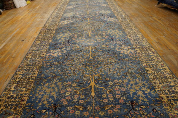 Intricate blue runner rug with a yellow tree-of-life and floral motif resting on worn wood flooring.