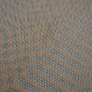 Close-up geometric rug texture with cream chevron stripes alternating with textured pale blue woven patterns.