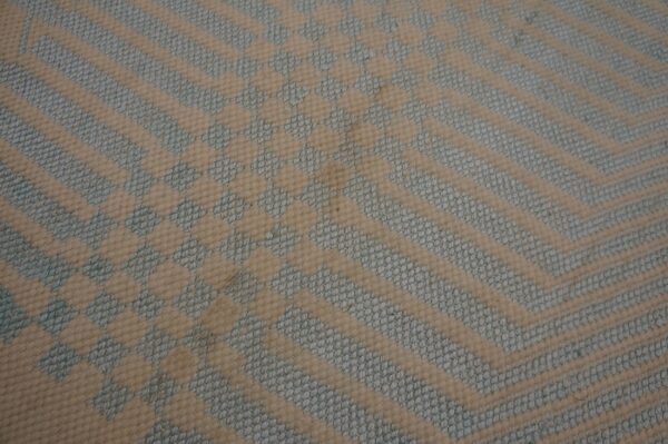 Close-up geometric rug texture with cream chevron stripes alternating with textured pale blue woven patterns.