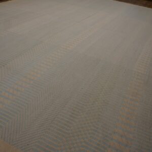 A large low-pile beige and pale blue rug displaying a repeating angular chevron pattern on wood flooring.