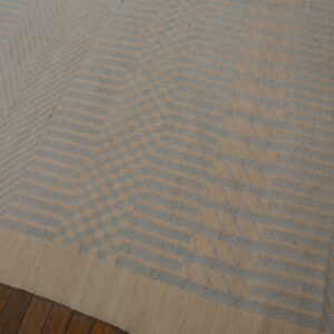 Low-pile rug in beige and light blue featuring a geometric chevron pattern on dark wood floorboards.